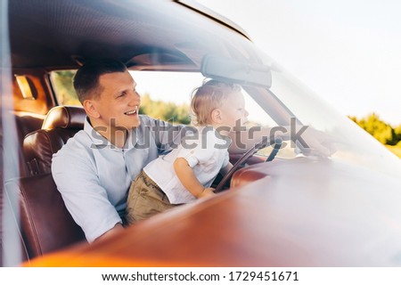 Buick Riviera in retro style. Unique car. Cute blond boy is sitting behind the wheel of a retro car with his father.