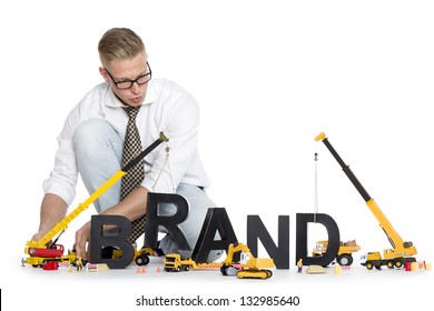 Build Up A Brand Concept: Focused Businessman Building The Word Brand Along With Construction Machines, Isolated On White Background.