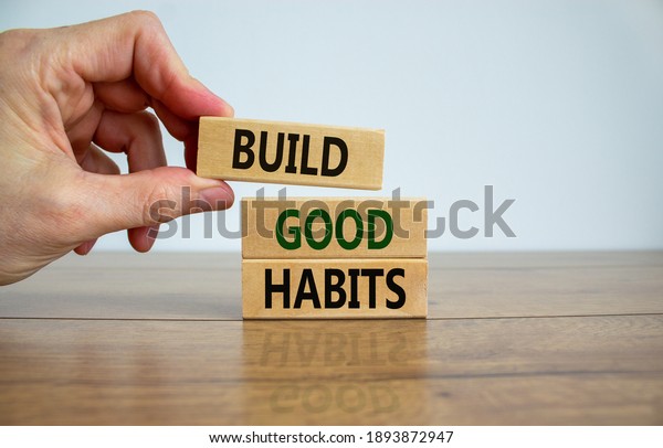 Build good habits symbol. Wooden blocks with\
words \'build good habits\'. Male hand. Beautiful wooden table, white\
background, copy space. Business, psychological and build good\
habits concept.