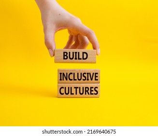 Build Inclusive Cultures symbol. Wooden blocks with words Build Inclusive Cultures. Beautiful yellow background. Businessman hand. Business and Build Inclusive Cultures. Copy space.
