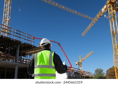 builder architect engineer foreman worker with hard hat and safety vest on major construction site with crane in background checking plan