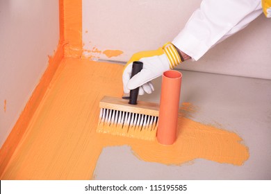 Builder With Brush Applies Waterproofing On The Floor Of The Bathroom