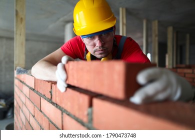 Builder Carefully Puts Red Brick On The Masonry. Quick Work Bricklayer. Guy Measures Level Masonry. Man Is Building Brick Wall. Correctly Calculate Material. Builder Manually Carries Brick Structure