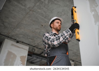Builder checking vertical alignment of drywall panel using spirit level during building construction