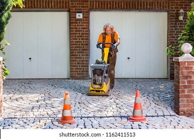 Builder Or Contractor Laying New Paving Bricks In A House Driveway Using A Mechanical Compacter For Compaction Of The Cement Pavers.