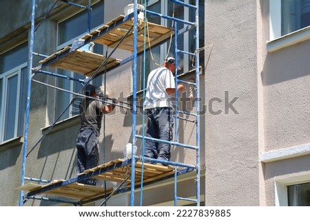 Builder contractors painting external walls outside house facade. Close up on painting house outside wall.
