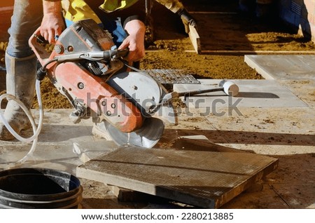 Builder cutting concrete slabs with petrol concrete saw and a diamond blade during external footpath paving works close up