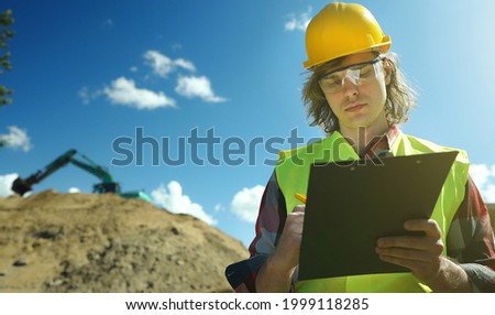 Builder with documents on the background of a road junction construction site.