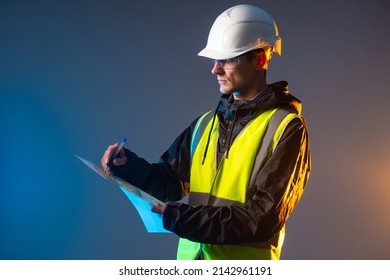 Builder draws blueprints. Construction company manager. Man holding construction blueprint. Room drawings in hands of engineer. Architect in yellow vest. Builder in protective helmet. Builder on dark