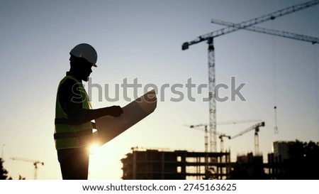 Builder, engineer or architect in helmet checking drawings at construction site. Silhouette of foreman, industrial building, engineering house industry, inspector examining plan of buildings