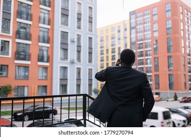 A builder or engineer, stands with his back, looks at buildings, in a suit, talks on the phone, a skyscraper