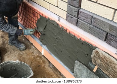 A Builder Faces The Basement Of A House With A Wild Stone. Flat For Cladding, Tabata On The Construction Site.