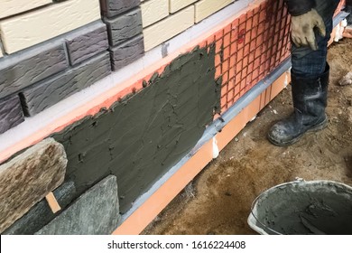 A builder faces the basement of a house with a wild stone. Flat for cladding, tabata on the construction site.