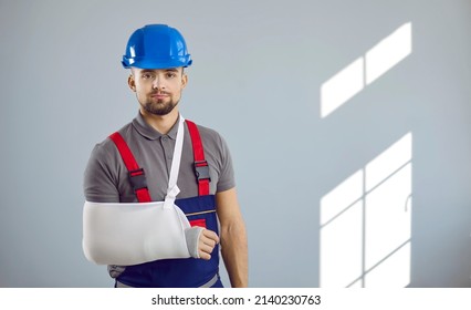 Builder Gets Injured At Work. Portrait Of Man In Workwear Uniform, Hard Hat And Sling Immobilizer On Broken Arm Standing On Copy Space Wall Background. Accident And Injury At Construction Site Concept