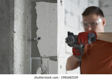 A builder with glasses drills a hole in the wall to see through. The master man makes a hole in the wall with a percussion drill. Construction drill drill for concrete creating a hole.