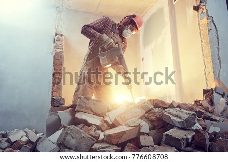 builder with hammer breaking wall indoors
