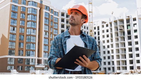 Builder In Hard Hat Holding Clipboard On Construction Site