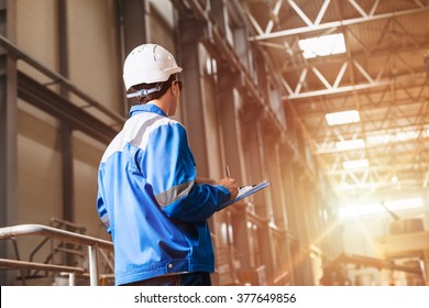 Builder In Hard Hat Looking At An Industrial Interior. Metal Smelting Plant