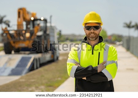 Builder in helmet with excavator for construction at the construction site. Machinery tractor with builder at buildings background. Excavator loader tractor and buider worker.