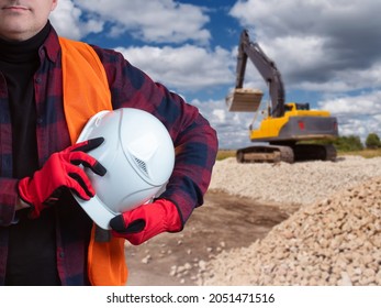 Builder With Helmet In Hand. White Helmet In Hand Of Builder. Man Near Excavator. Concept - Stone Mining. Worker Next To Stone Excavator. Male Worker Of Stone Quarry. Selective Focusing.