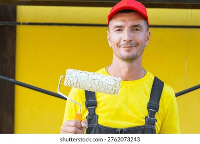 Builder holding paint roller, standing in front of house, wall painting and home improvement, handyman private service, tools for at-home repairs.