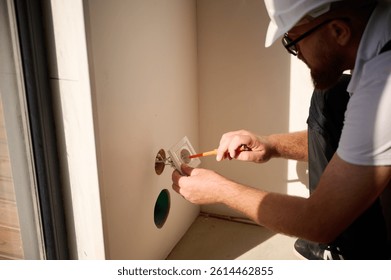 Builder installing electric socket in new apartment. Installing electrical wall outlets with a screwdriver in a new home. Electrician repairing power socket, electrician mounting wiring for sockets