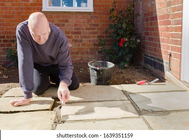 Builder Laying And Grouting York Stone Paving Slabs Outdoors, DIY Home Patio Project , UK