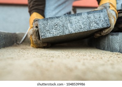 Builder Laying A Paving Brick Placing It On The Sand Foundation With Gloved Hands.