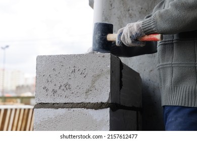 Builder Makes A Concrete Wall With Cement Blocks On The Construction Site Of A House. Concept Of Building A House. Leveling And Compacting The Masonry Blocks With A Rubber Mallet.