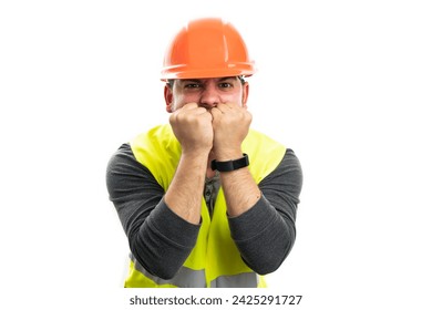 Builder man with angry desperate expression wearing fluorescent vest and orange helmet using fists to cover mouth gesture isolated on white background