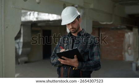 Builder man architect engineer in hard hat inspecting building construction writing checklist note plan industry Caucasian guy male technician repairman foreman inspector developer check build project