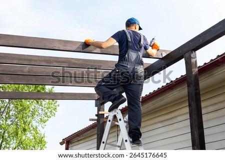  builder man with electric screwdriver installing impregnated wooden board. man  builds a wooden terrace near his house.