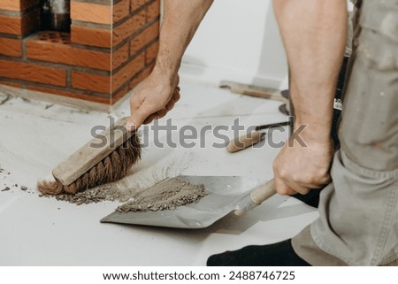 A builder man sweeps up construction debris with a broom.