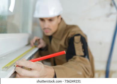 Builder Measuring A Window Using A Tape Measure And Pencil