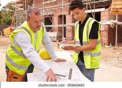 Builder On Building Site Discussing Work With Apprentice