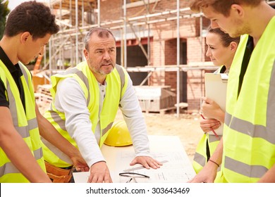 Builder On Building Site Discussing Work With Apprentice