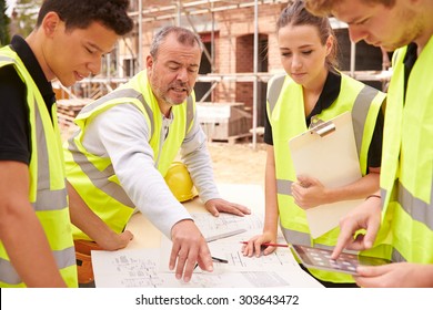 Builder On Building Site Discussing Work With Apprentice