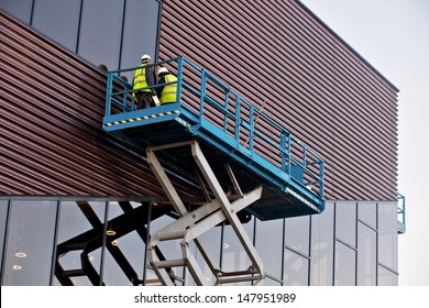 Builder On A Scissor Lift Platform At A Construction Site. Men At Work