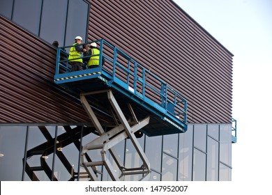 Builder On A Scissor Lift Platform At A Construction Site. Men At Work