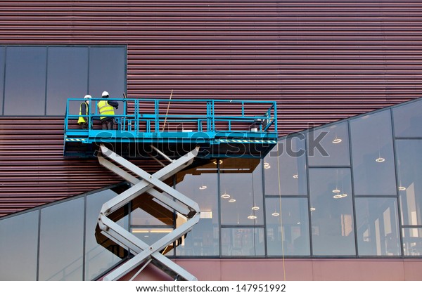 Builder on a Scissor Lift Platform at a construction\
site. Men at work