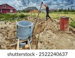 Builder places one concrete ring on top of another and levels it with lever using steel pipe when building septic tank.