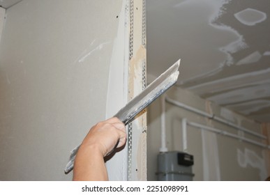 Builder plastering, skim coating, finishing, applying the first coat of plaster on a drywall partition wall  during house renovation.  - Shutterstock ID 2251098991