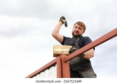 Builder Pounding Fence Post With Hammer In Summer