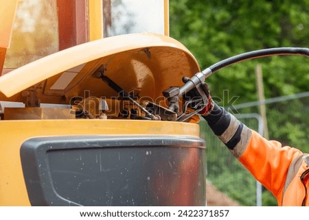 Builder in safety gloves filling excavator with diesel fuel on building site