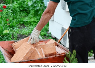Builder stacks red bricks in wheel barrow. Wheel barrow full of stacked bricks.