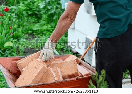 Builder stacks red bricks in wheel barrow. Wheel barrow full of stacked bricks.