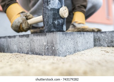 Builder tamping down a new paving slab or brick with a large mallet in a close up view on the hands and tool.