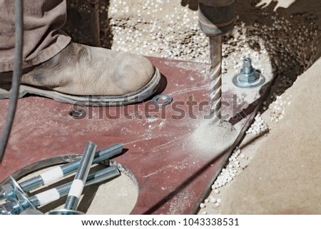 The builder uses a drill to make holes in a concrete