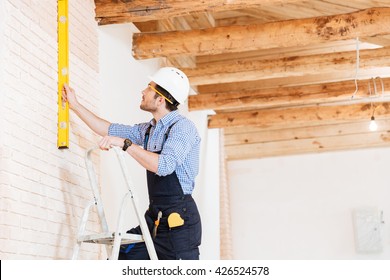Builder using consruction level and standing n the ladder at the working area