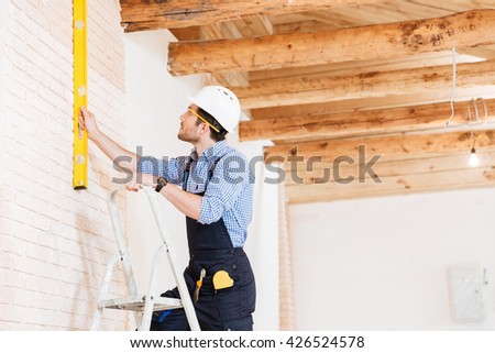 Builder using consruction level and standing n the ladder at the working area